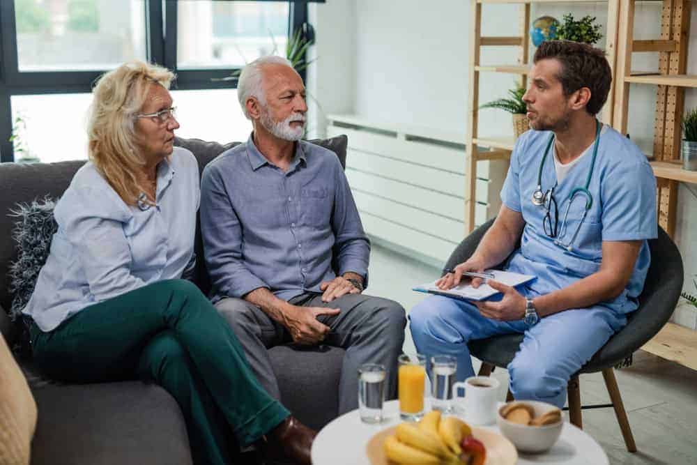 A couple talking to a male doctor during a home visit.| palliative care