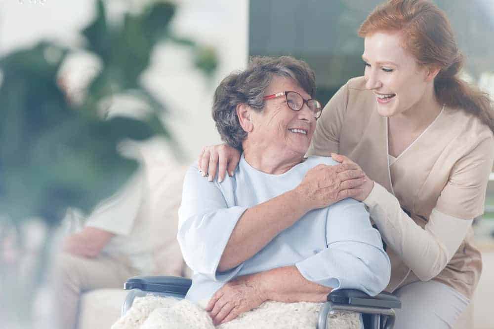 Elderly woman smiling and hugging her specialized hospice caregiver | what are the goals of hospice care