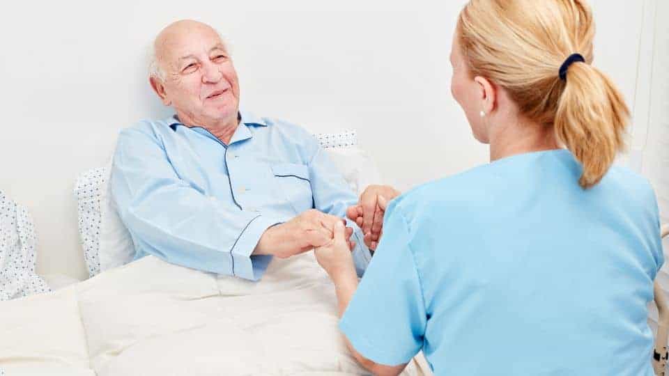 A nurse holding a sick man’s hand and comforting him. | Hospice care