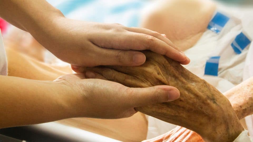 A caregiver holding the hand of a senior woman.