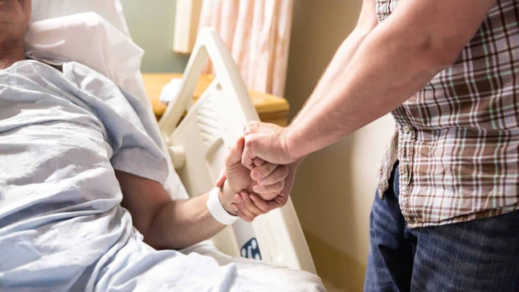 a caregiver holding the dying hand of a patient in end-of-life care