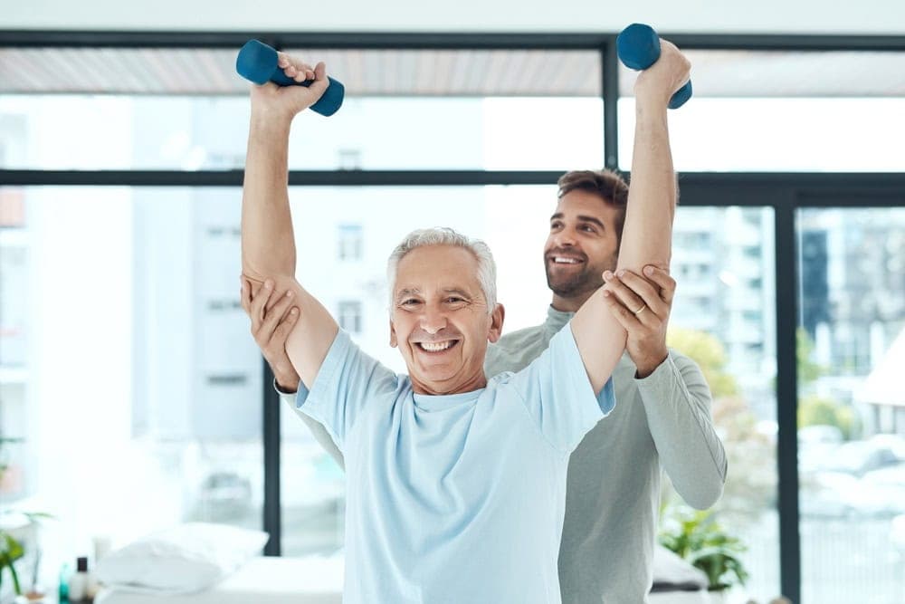 A male physical therapist guiding a senior man in exercising