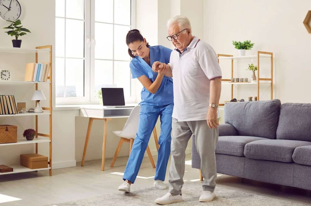 A female physical therapist guiding a senior man how to walk after a stroke attack