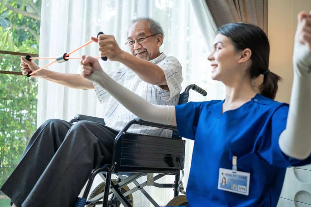 A female physical therapist teaching a senior man in a wheelchair how to stretch a band