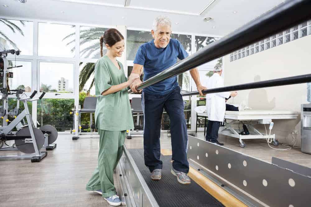 Physical therapist helping a male patient walk between parallel bars in a physiotherapy clinic