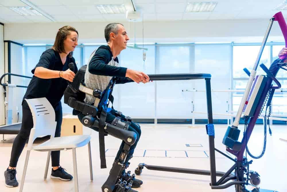 physiotherapist helping a man sit using a robotic exoskeleton in a physiotherapy clinic