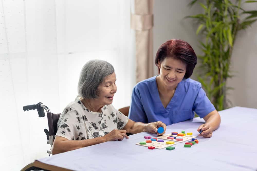 Alzheimer’s nursing home - senior woman playing puzzles with caregiver