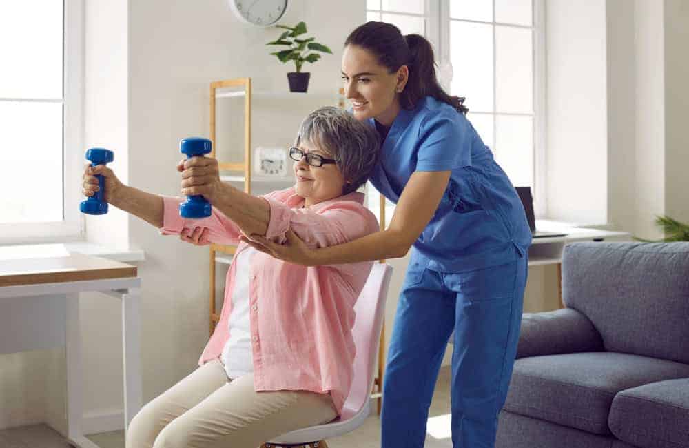 Young nurse and elderly woman performing physical therapy exercises