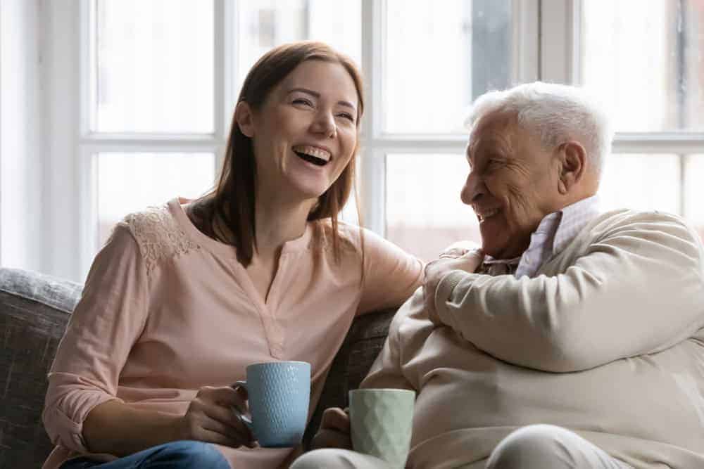 A senior resident and their caregiver laughing while enjoying some coffee.