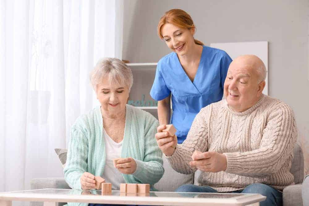 A senior couple in an assisted living having fun playing a game while being accompanied by their caregiver.