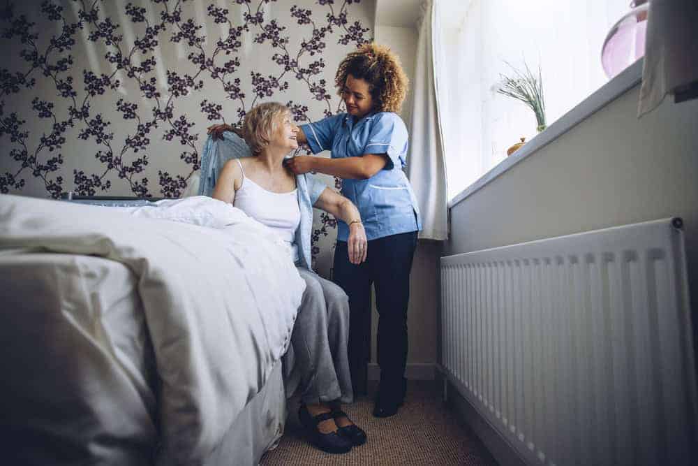 A caregiver helping a senior woman resident change into fresh clothes.