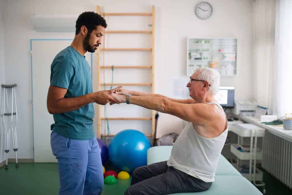 A male physical therapist helping a senior man stretch