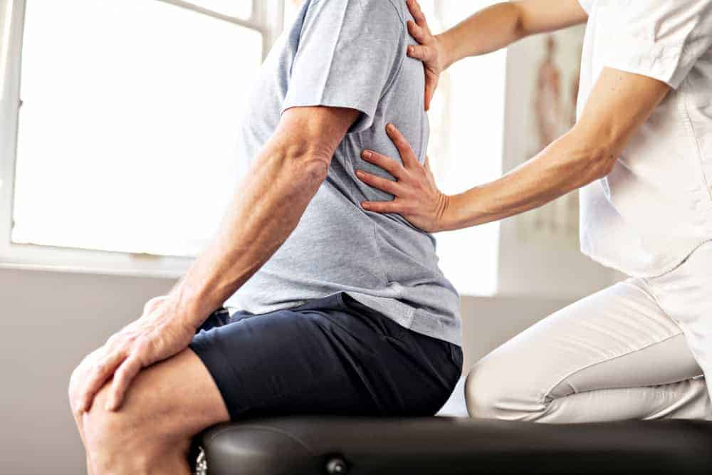 A therapist’s hand massaging a senior’s back