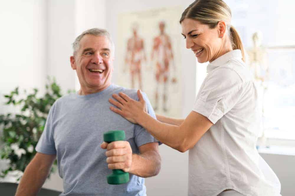 A female therapist and senior old man happily doing the exercise routines