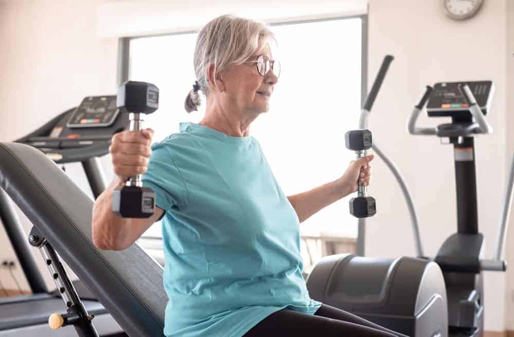 physical therapist and kinesiology - an older adult lifting weights in a gym as part of her individualized plan