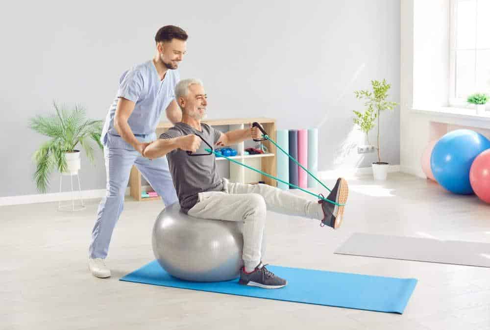 A therapist guiding a senior man in doing his exercise.