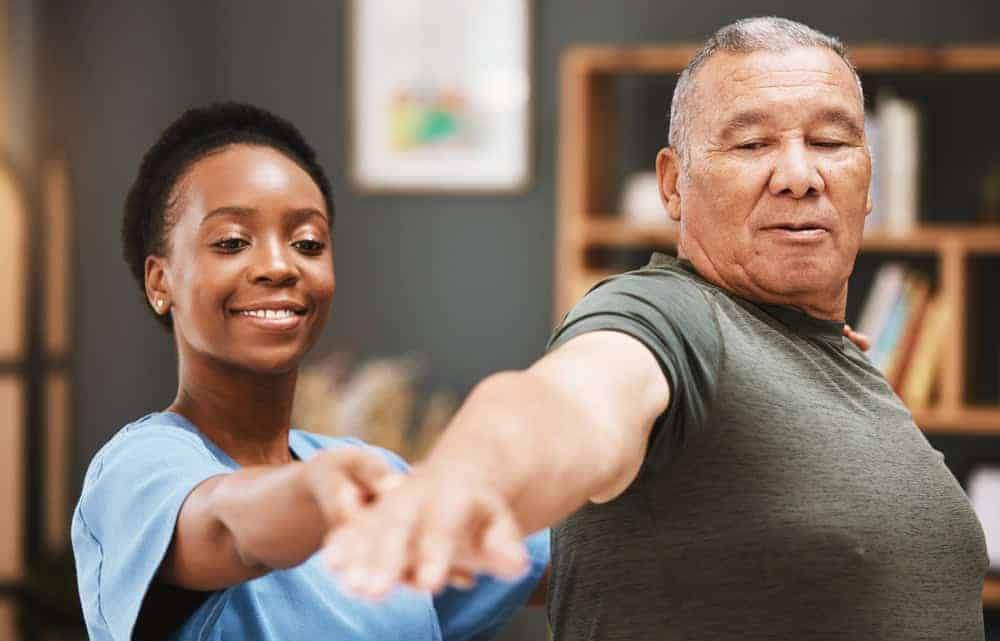 Black caregiver aiding senior with physiotherapy for his shoulder and back