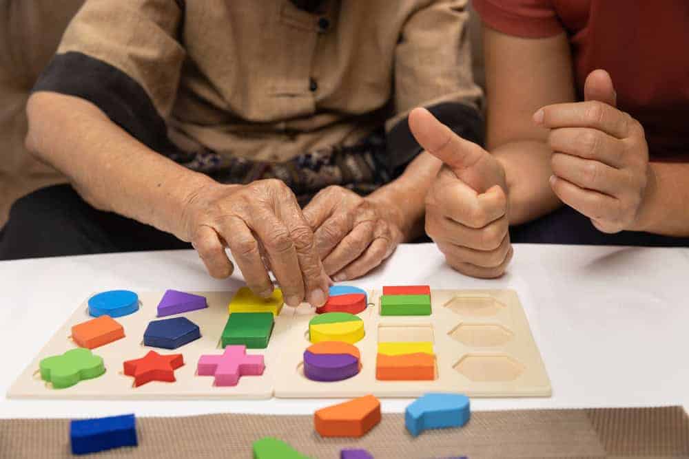 Caregiver playing puzzles with elderly as a memory care activity - can someone with dementia live in assisted living