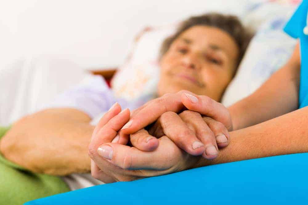 Caregiver holding hands of an elderly person in bed - private home care for seniors