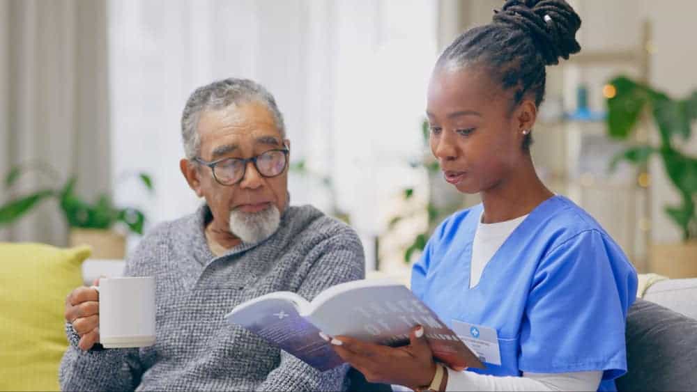 Female caregiver reading a book to an elderly man at home - private in-home care