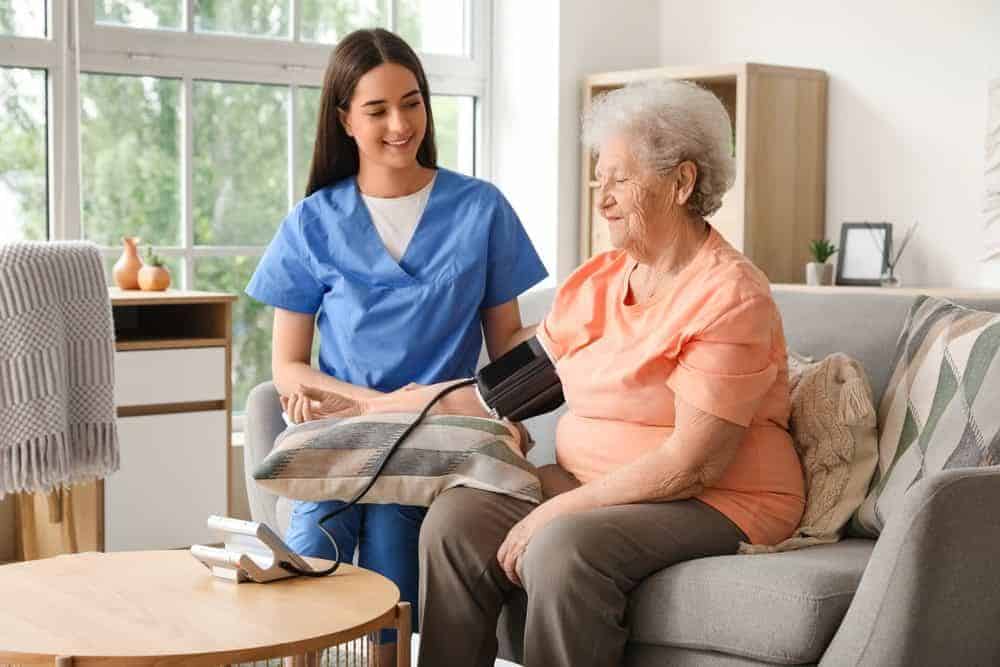 a smiling female home health caregiver measuring a senior woman’s blood pressure at home