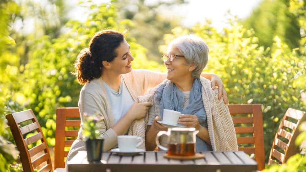 A female caregiver drinking tea with elderly woman outdoors - in-home health care