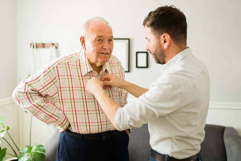 a male caregiver helping a senior man get dressed - home health care