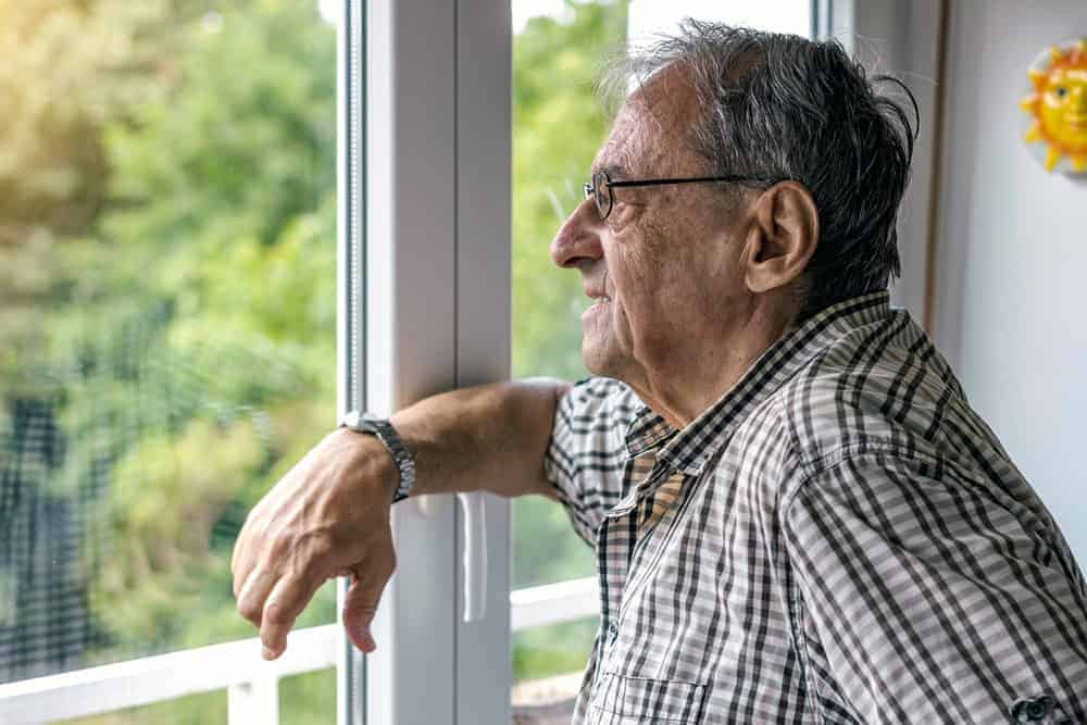 Elderly man looking outside the window and sad - personal care at home