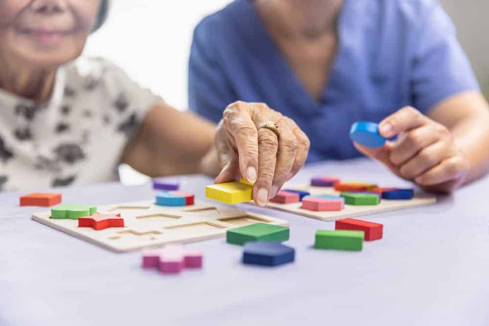 Elderly woman and caregiver solving puzzles - memory care facility cost