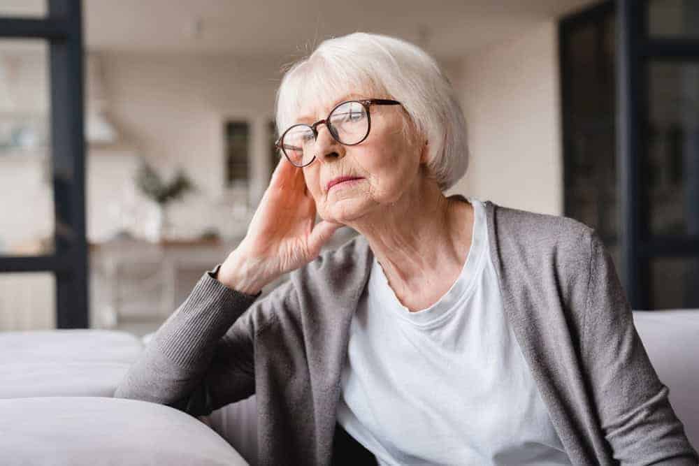 Sad elderly woman looking outside the window in a memory care unit