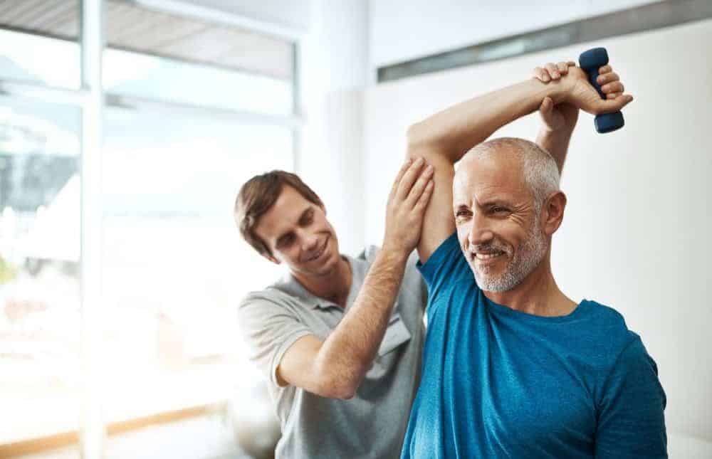 a physiotherapist helping a senior with his physical therapy exercises at a long term health facility