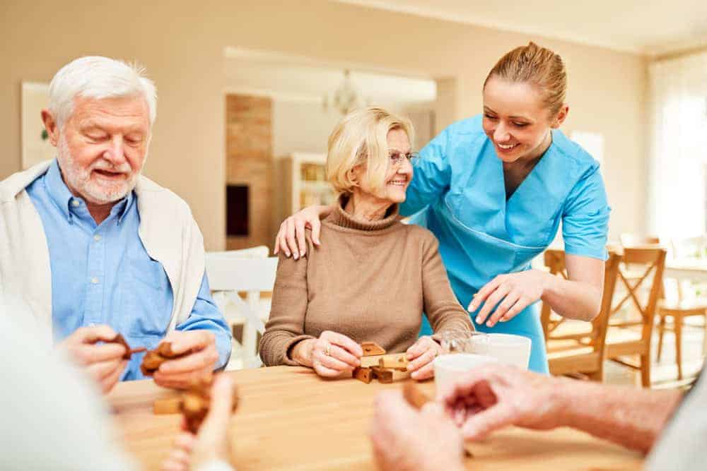 Happy seniors sitting around a table with their caregiver in an independent assisted living home