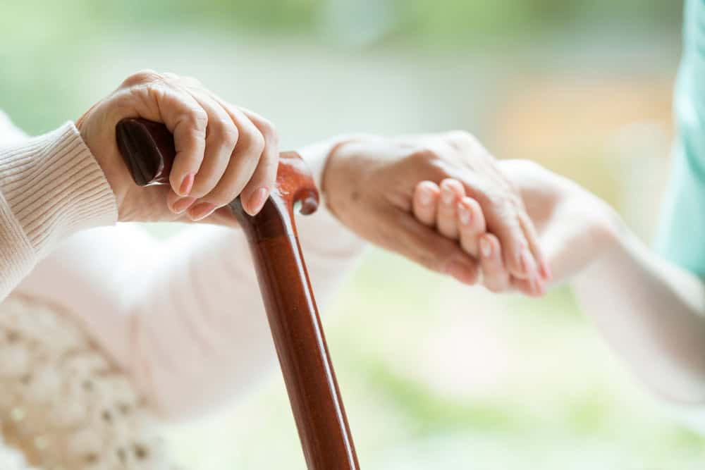 a senior holding a walking stick and a caregiver’s hand