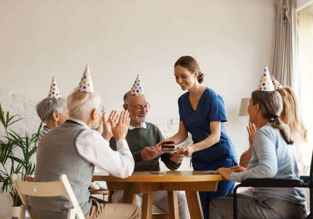 Senior men and women wearing party hats having fun with elderly caregivers