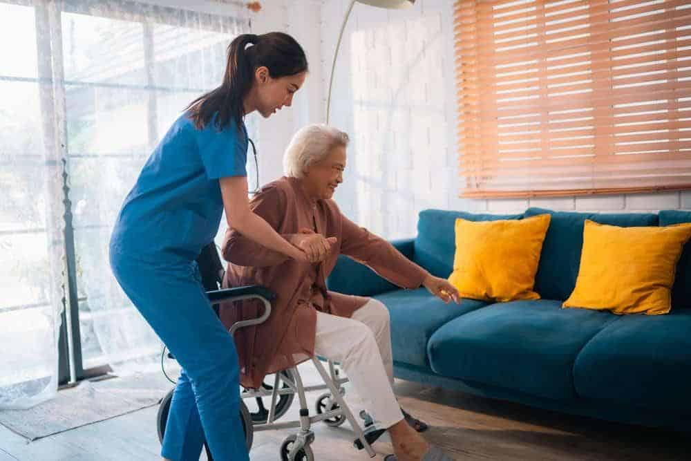 caregiver assisting a senior woman to get up from a wheelchair - home support