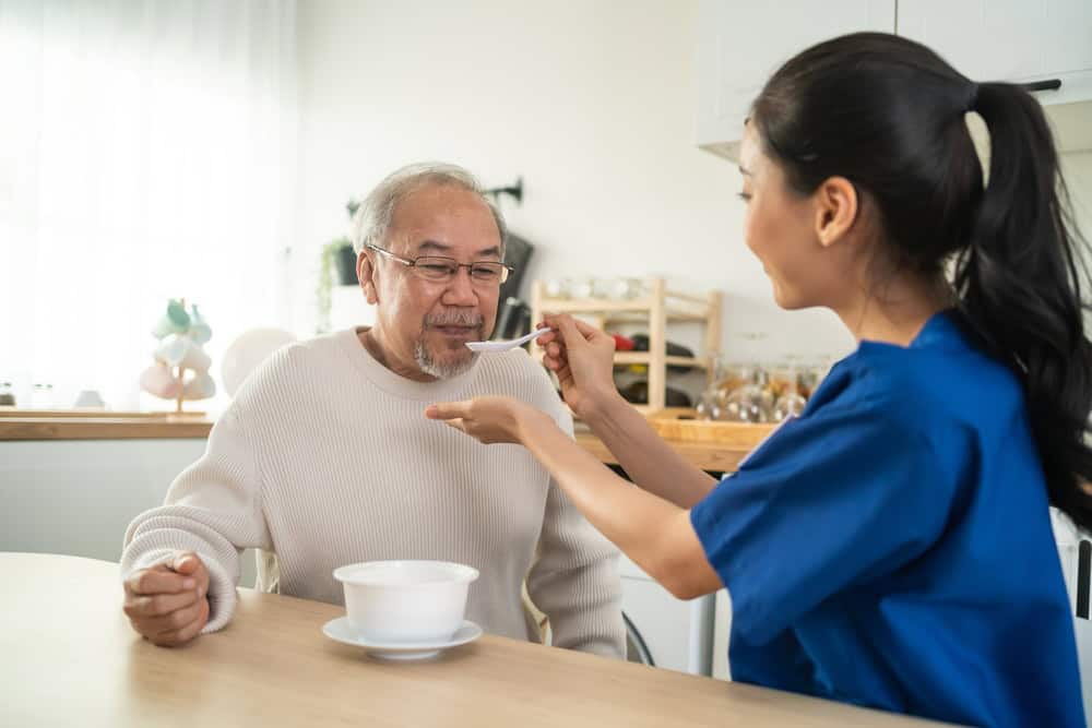 a young in-home caregiver helping a client with his meal at his home