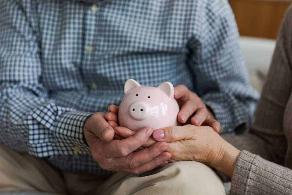 Hands of a senior couple holding a piggy bank | inhome care services cost