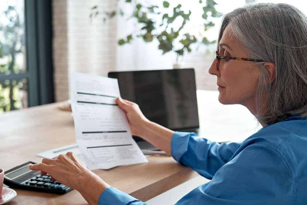 A senior woman holding a paper while calculating the cost of 24-hour home care | how much does private home care cost per hour