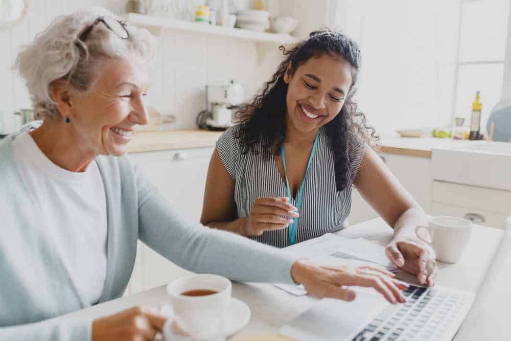 A volunteer woman teaching a senior woman how to use technology on a laptop | cost of in home care