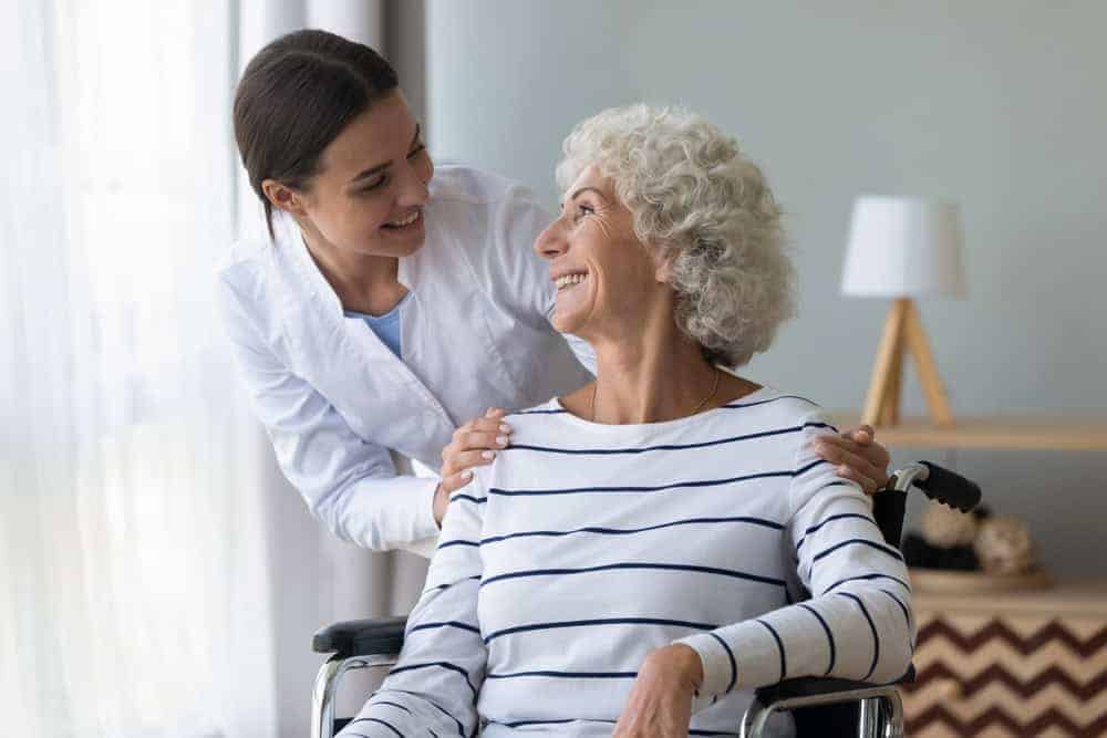 A female at-home care nurse smiling at a senior patient