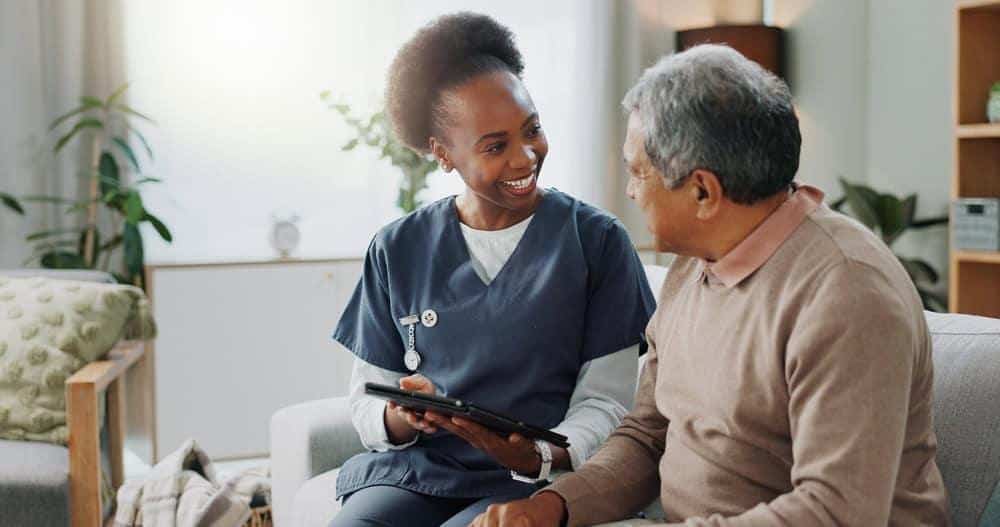 A female caregiver teaching a senior man how to use a tablet - at home healthcare