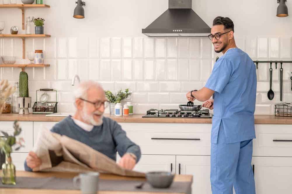 A man caregiver cooking for a senior man at home | at home home health care