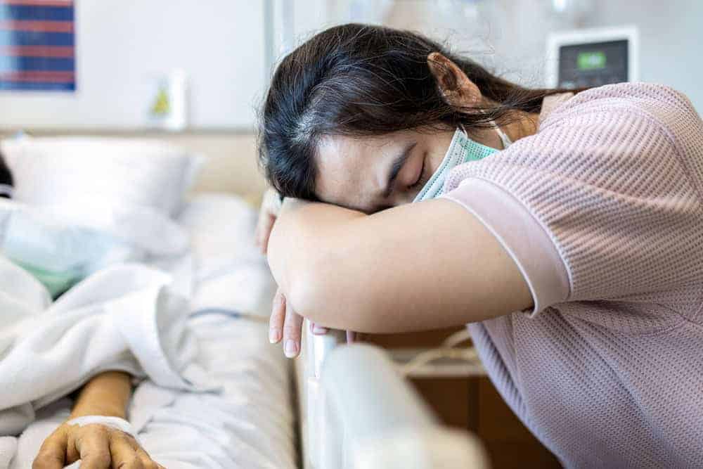 a family member fallen asleep next to a loved one’s hospital bed - overnight care for seniors