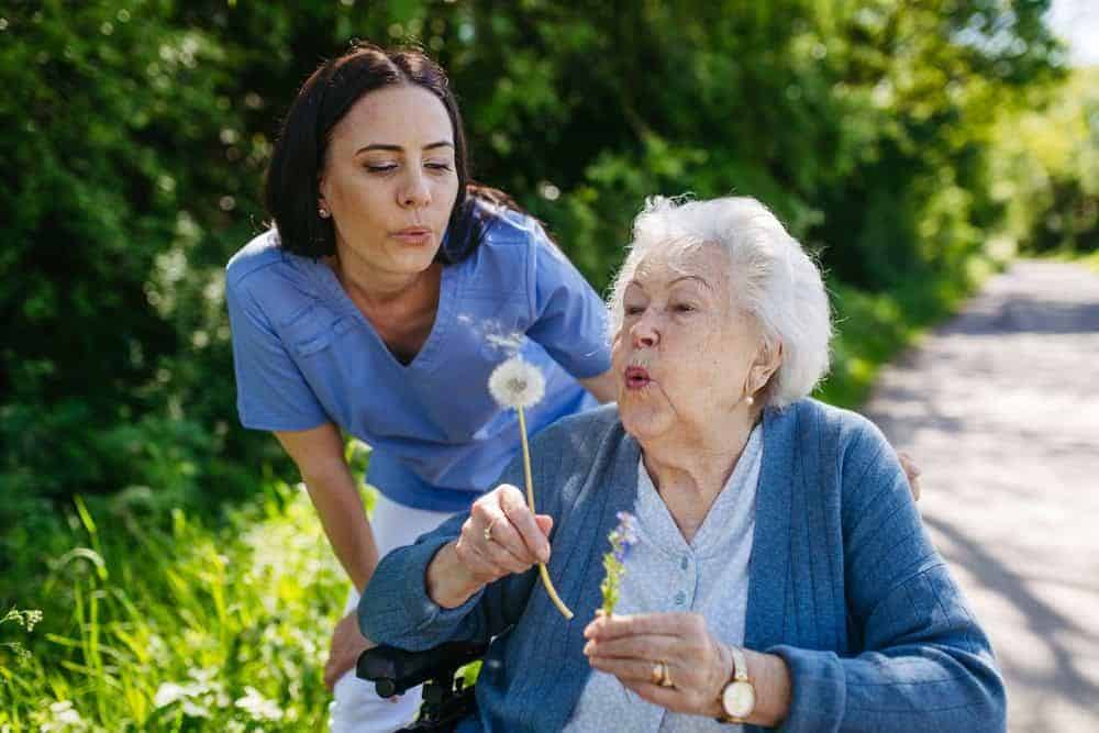 a nurse practitioner helping a woman in a wheelchair enjoy her garden