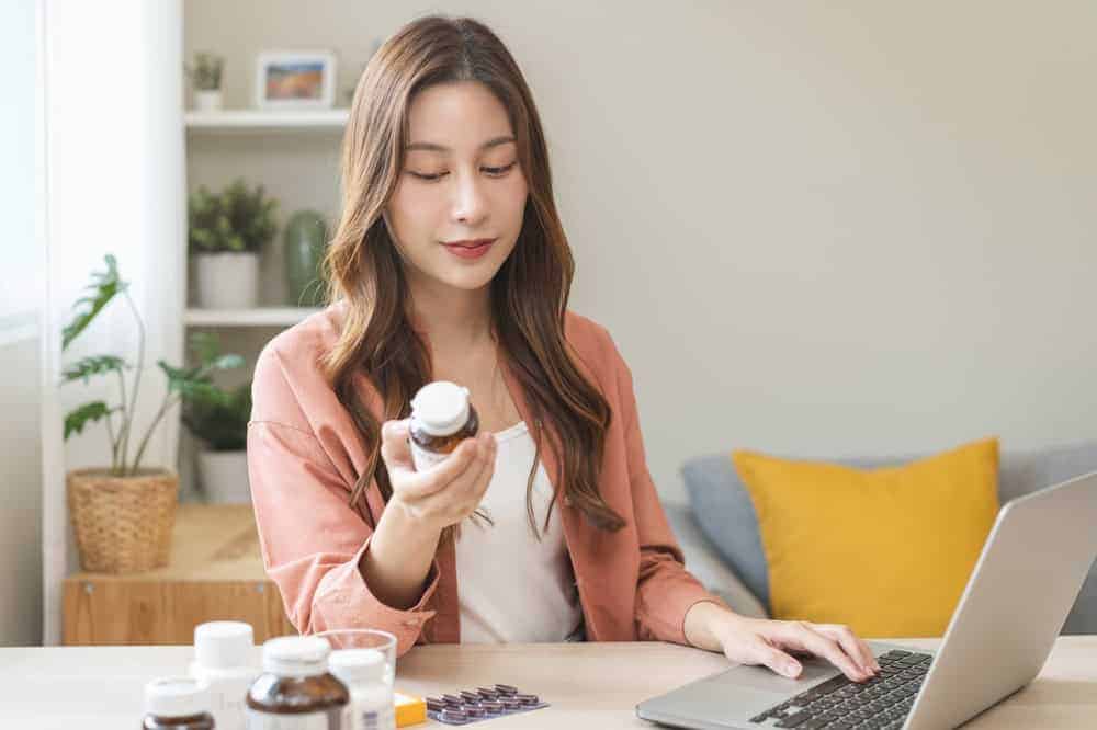 A woman holding a tablet supplement bottle and reading the label