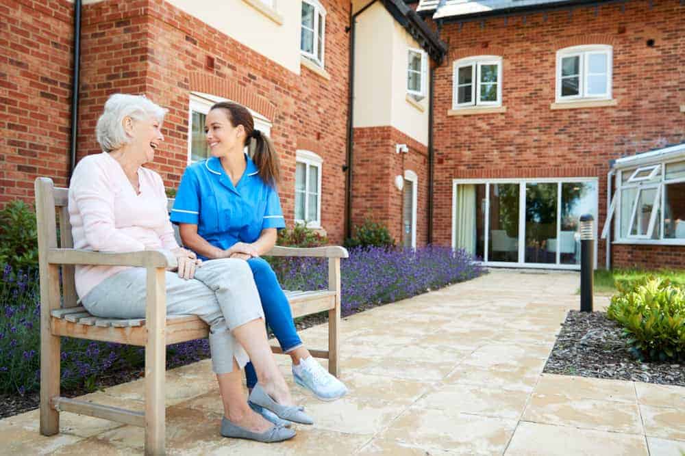 senior woman sitting with a nurse in a nursing home’s yard