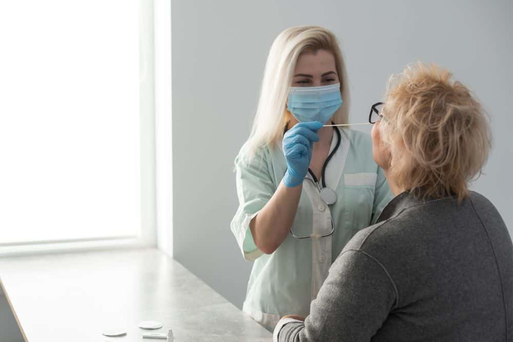 a staff member wearing personal protective equipment obtaining a swab from a resident