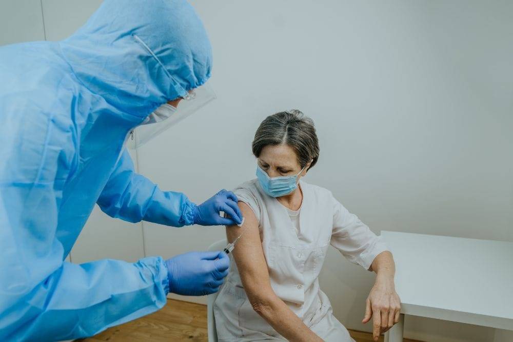 an employee in full PPE administering an injection to a senior wearing a mask