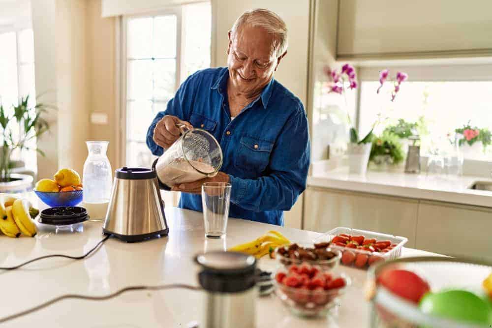 elderly man holding a glass of Ensure smoothie