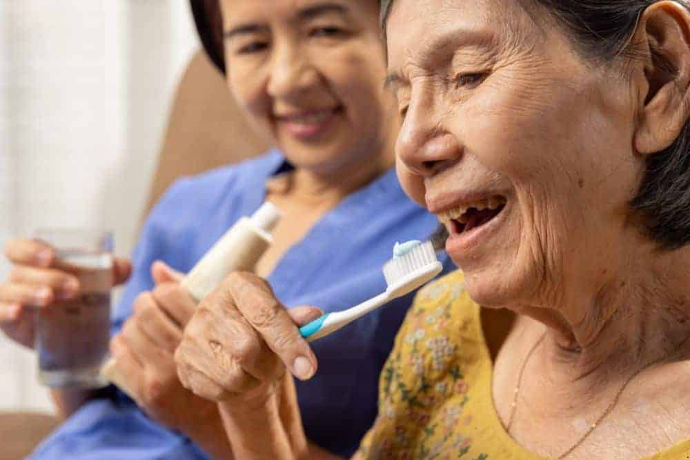 caregiver helping an elderly woman keep her oral hygiene by flossing